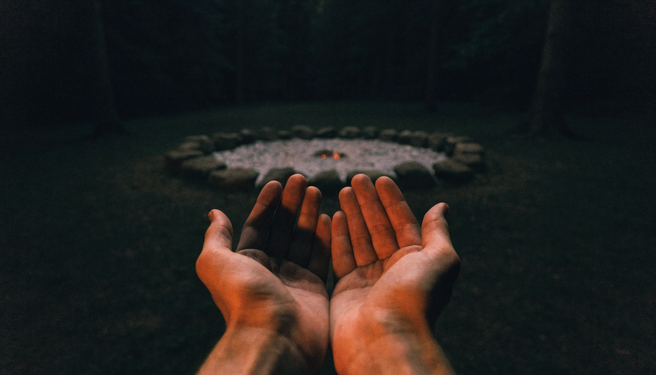 Two open hands held near the glowing embers of a fire circle